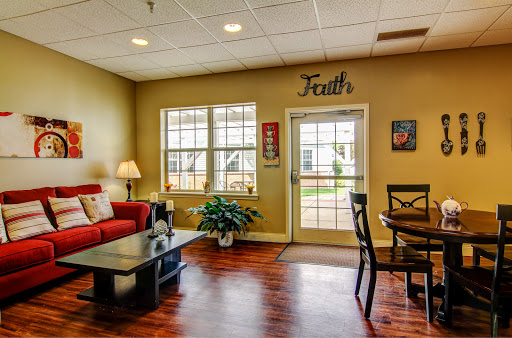 A cozy living room setup featuring a red couch, wooden table, and large windows that invite natural light.