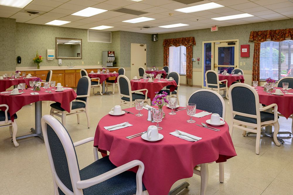 A neatly arranged dining area with tables covered in red tablecloths, set with cups and saucers.