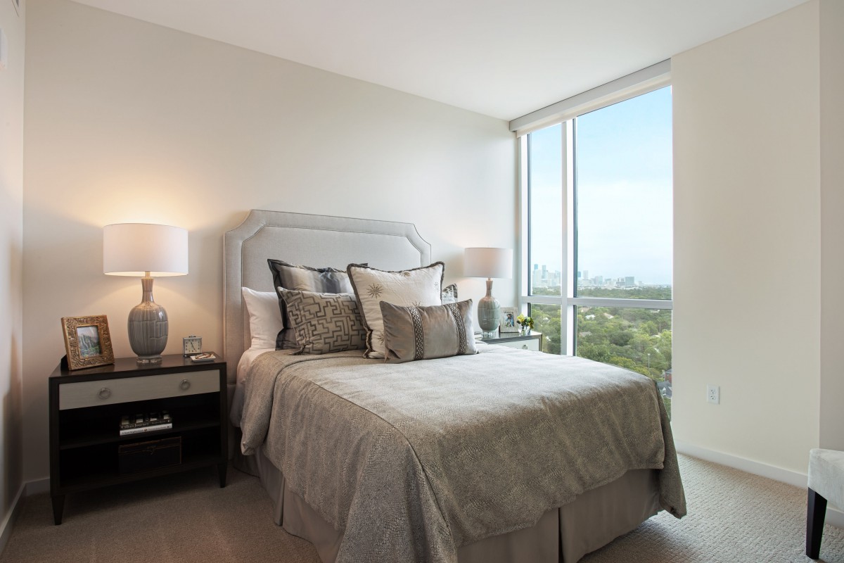 A modern bedroom featuring a cozy bed with decorative pillows, surrounded by natural light from large windows.