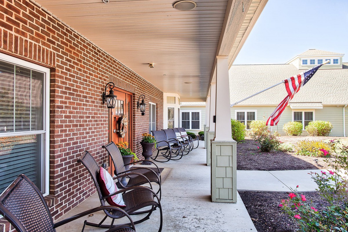 A cozy porch with chairs lined up against a brick wall, alongside a well-maintained patio area.