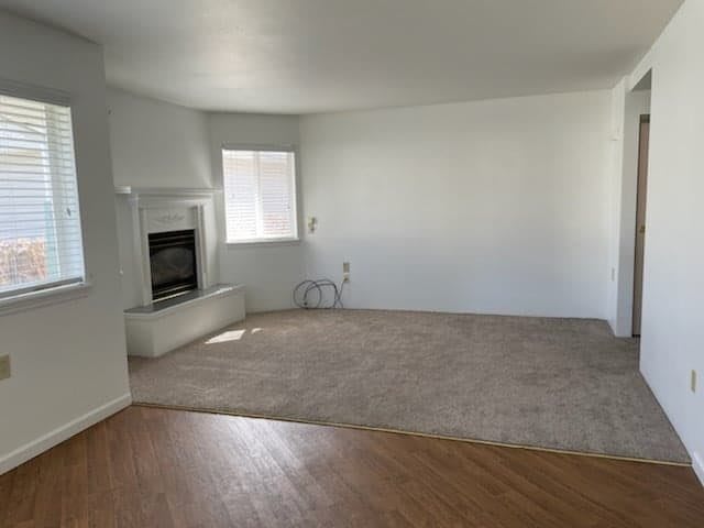 An empty living room with a fireplace, carpet and hardwood flooring.