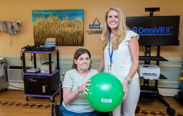 A therapist assists a patient with a green exercise ball in a rehabilitation setting.