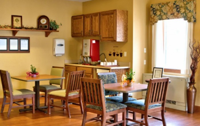 A cozy dining area with wooden tables and chairs, adjacent to a kitchen space.
