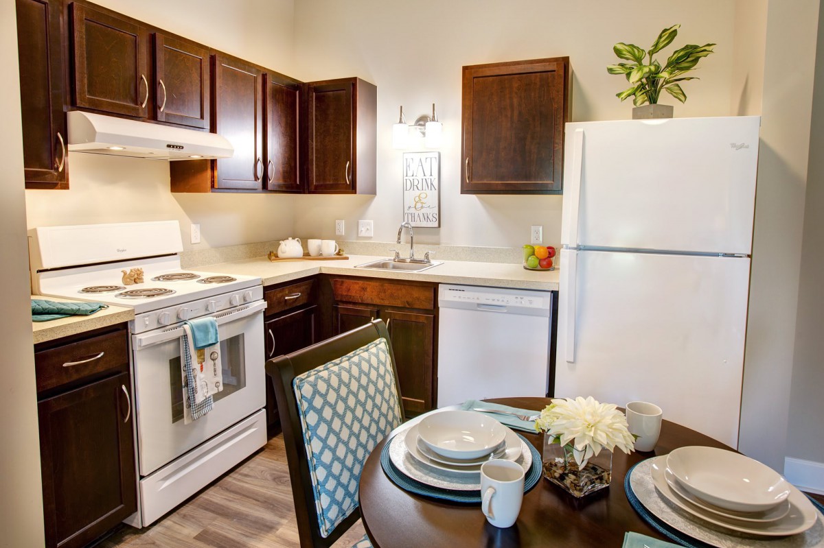 A cozy kitchen with dark wood cabinets, a dining table set for two, and modern appliances.