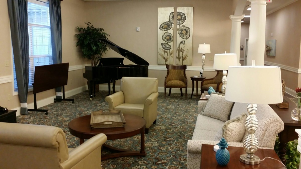 A cozy living room with a grand piano and comfortable seating, elegantly decorated with lamps and artwork.