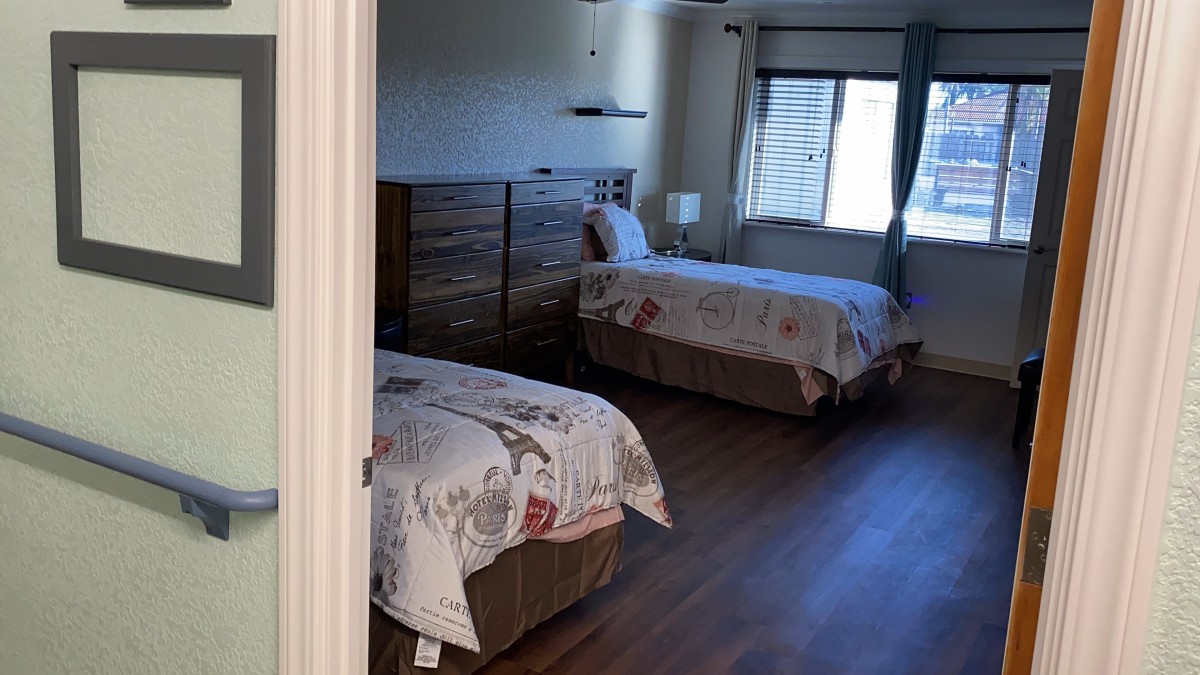 A cozy bedroom with two single beds, wooden furniture, and a window letting in natural light.