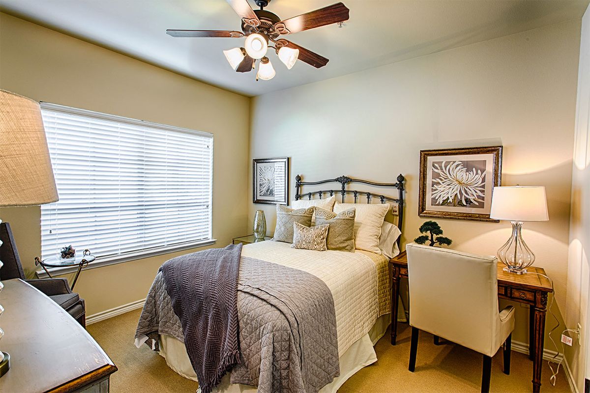 A cozy bedroom featuring a neatly made bed with pillows and a blanket, complemented by framed artwork on the walls and a ceiling fan overhead.