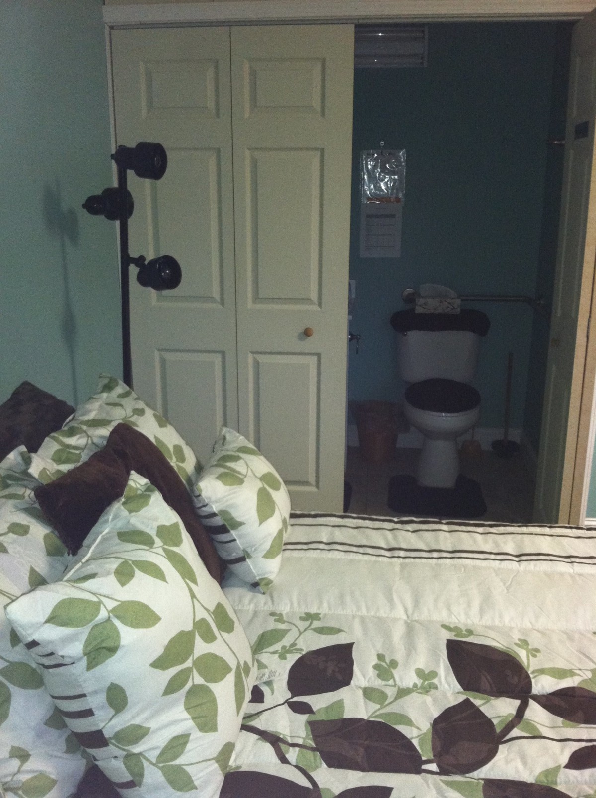 A bedroom with a floral-patterned bedspread, adjacent to a bathroom with a visible toilet.