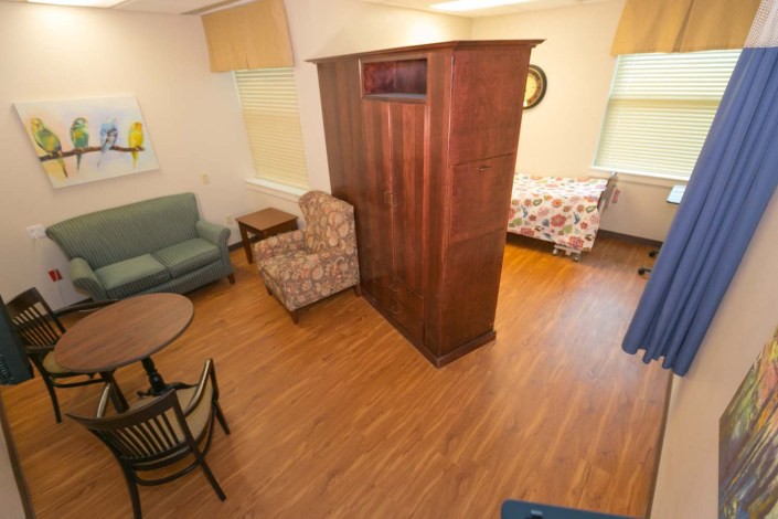 A cozy room with a sofa, chairs, table, and bed, featuring wooden floors and bright natural light.