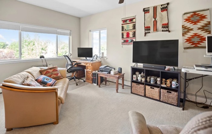 A cozy living room with a home office setup, featuring a TV, computer desk, and comfortable seating.