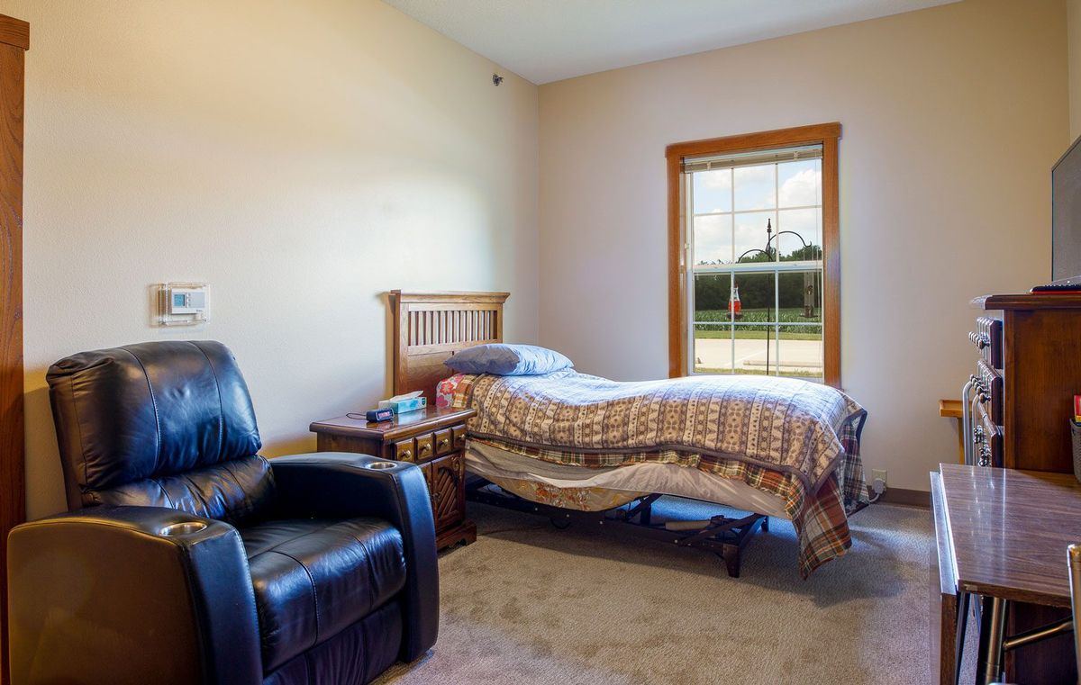 A cozy bedroom with a single bed and recliner chair near the window.