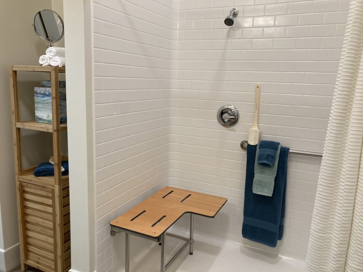 A bathroom shower featuring a wooden bench seat and blue towels.