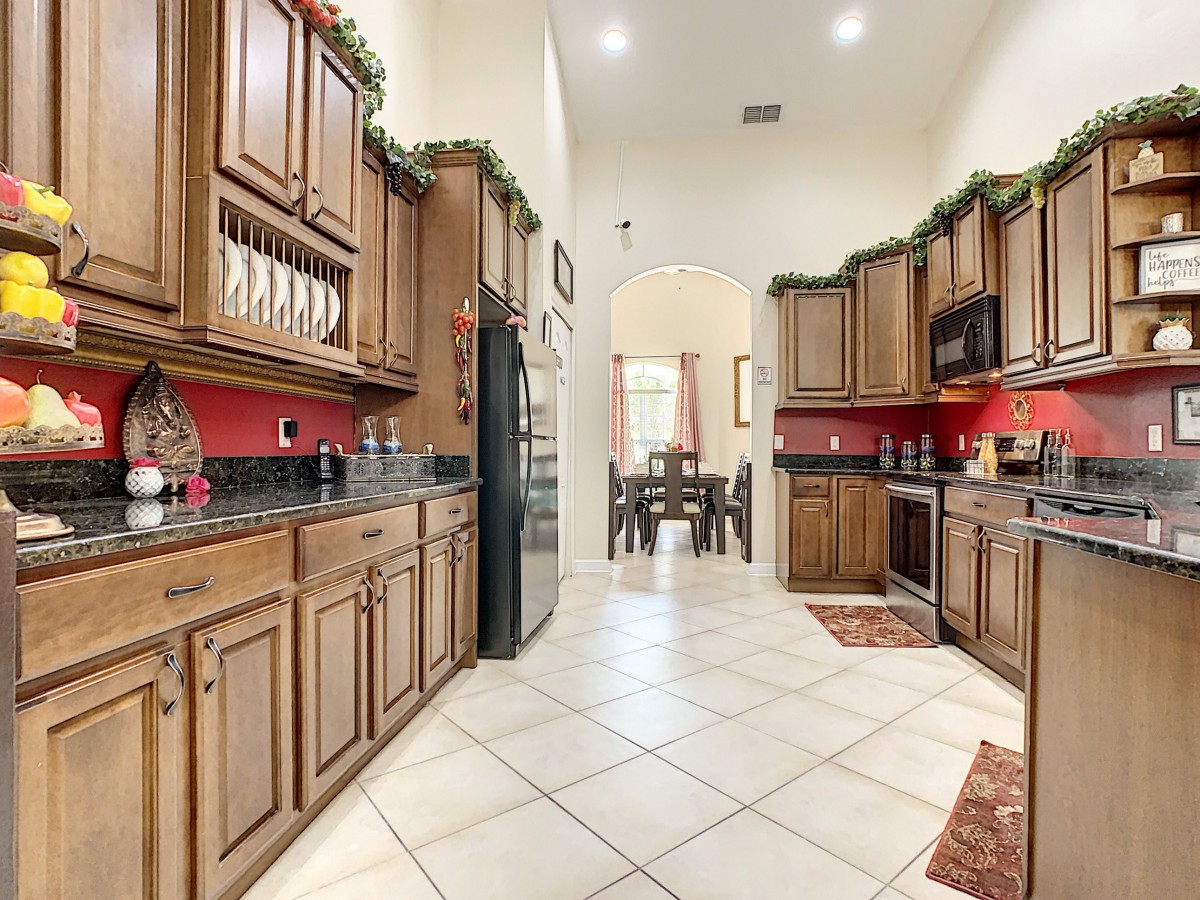 A spacious kitchen with wooden cabinets and red backsplash, featuring a tiled floor and decorative greenery.