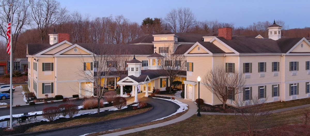 A large residential building with a winding driveway set against a backdrop of trees in the evening.