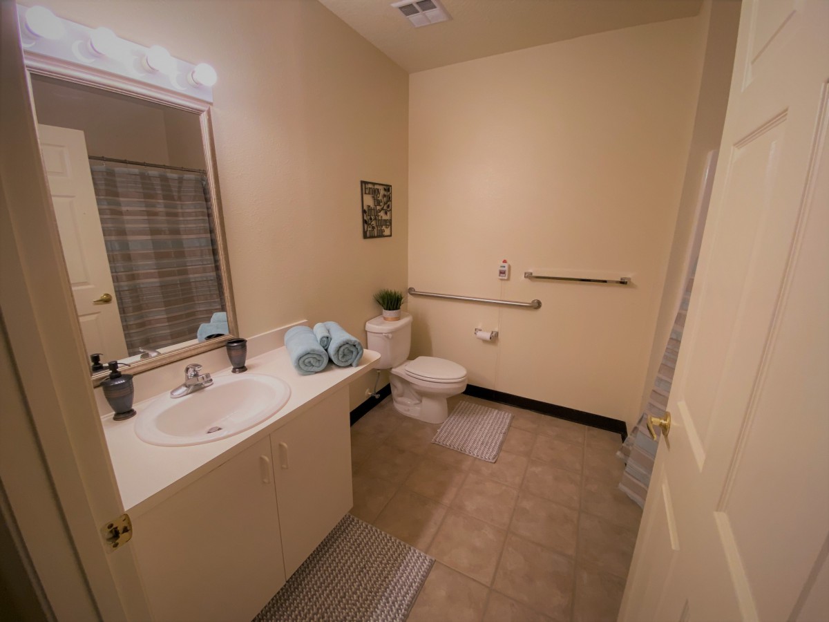 A bathroom with beige walls featuring a sink, mirror, and toilet.