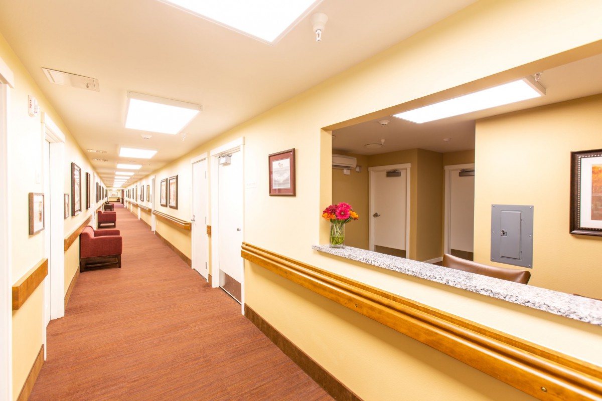 A brightly lit hallway with a reception area, featuring floral decor and comfortable seating.