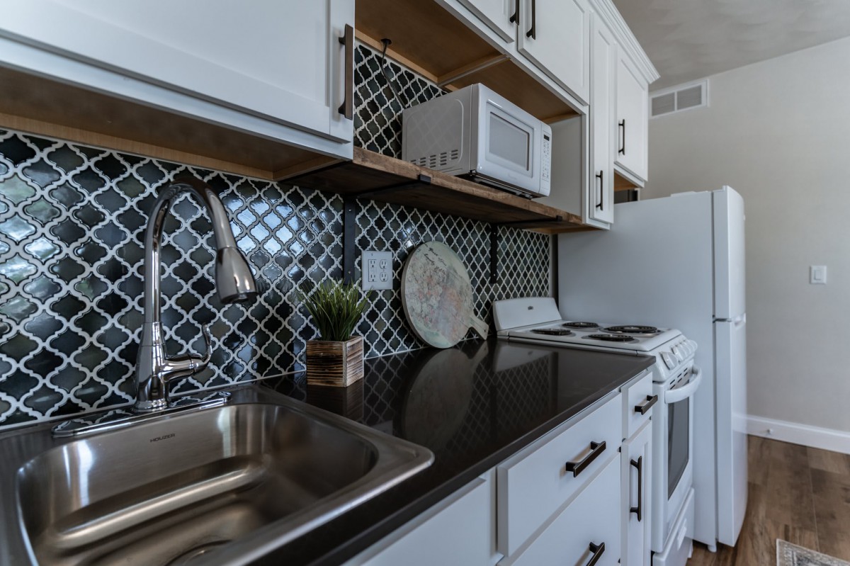 A modern kitchen with a black countertop, stainless steel sink, and geometric backsplash.