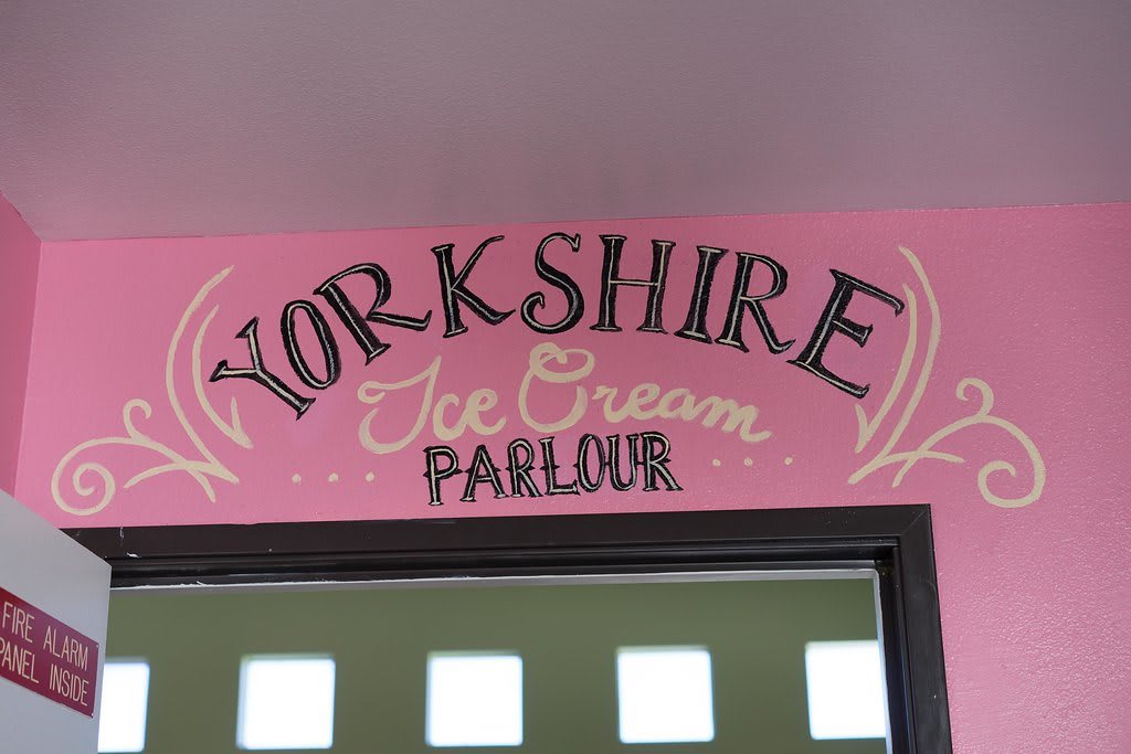 The image shows a sign for the Yorkshire Ice Cream Parlour with decorative lettering on a pink background.