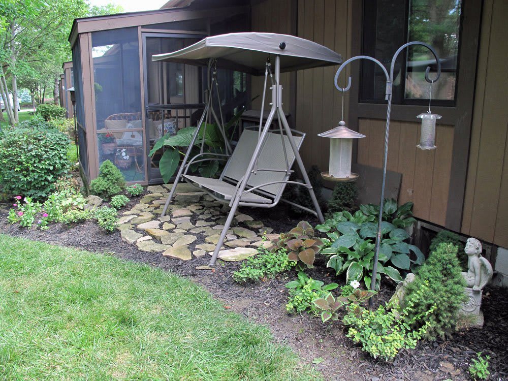 A cozy garden area featuring a swing seat with a canopy, surrounded by plants and landscaping, complete with a bird feeder.