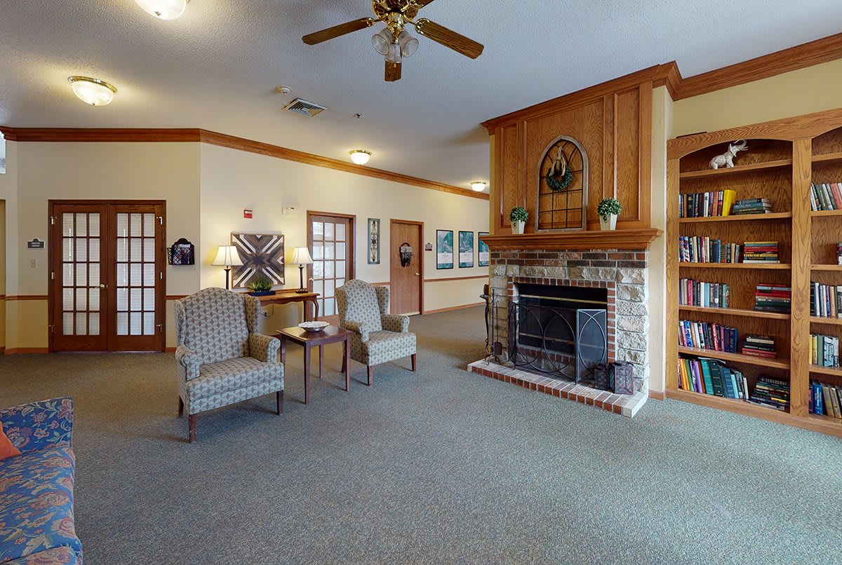 A cozy living room with a fireplace, comfortable chairs, and a ceiling fan.