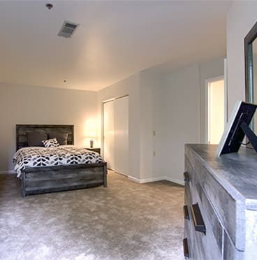 A spacious bedroom featuring a bed, dresser, and lamp in a modern interior setting.