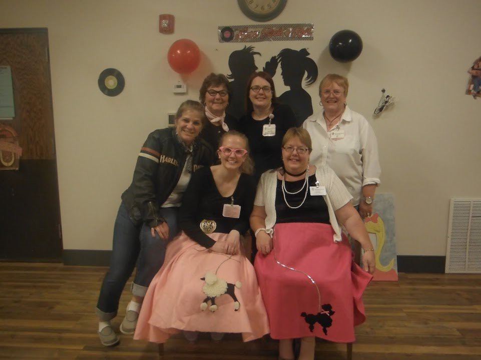 A group of people dressed in vintage-style clothing, including poodle skirts, smiling at a party.