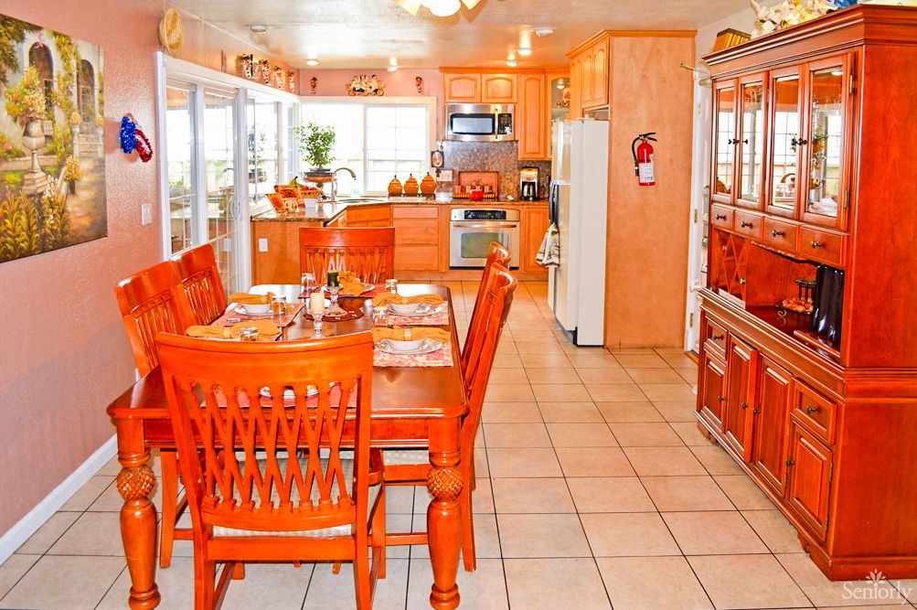 A bright kitchen and dining area featuring orange-toned wooden furniture and tile flooring.