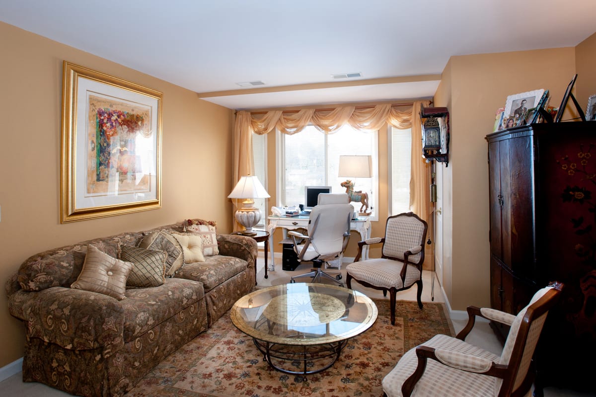 A cozy living room with an integrated office space featuring a sofa, chairs, coffee table, and desk by the window.