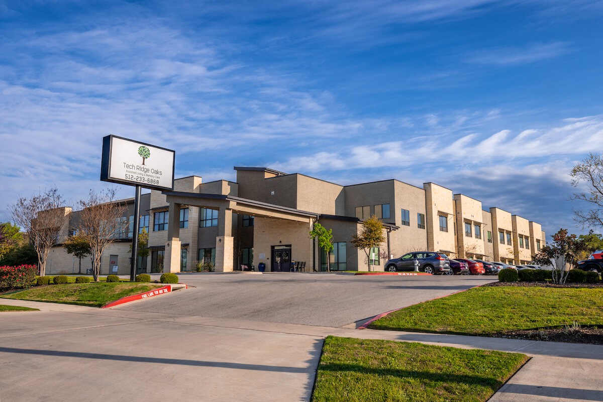 A modern commercial building with a parking lot under a clear blue sky.