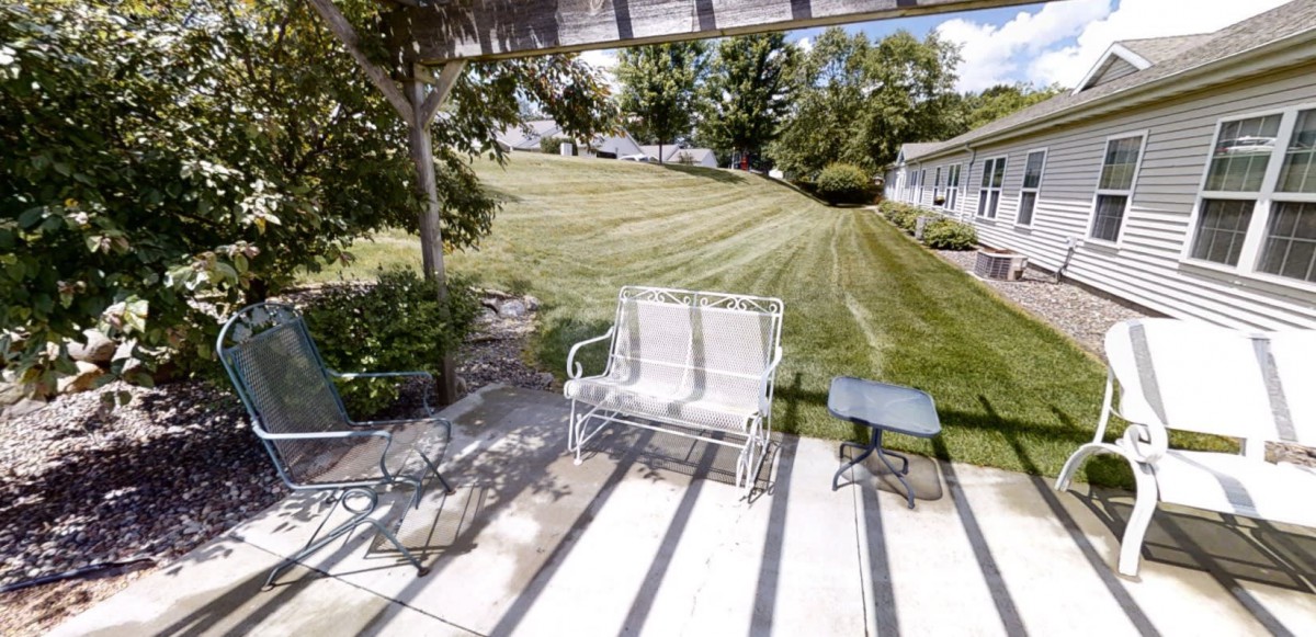 A peaceful backyard patio with a bench, table, and a well-manicured lawn.