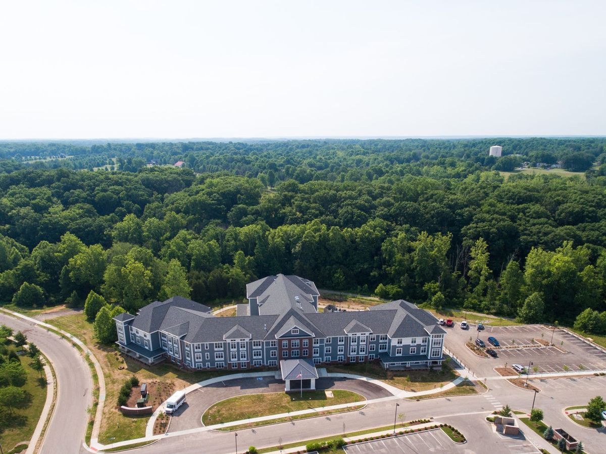 Aerial view of a large building surrounded by lush greenery and a parking lot.
