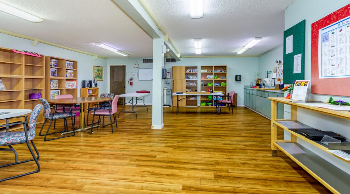 A well-organized classroom with wooden floors, tables, and shelves.