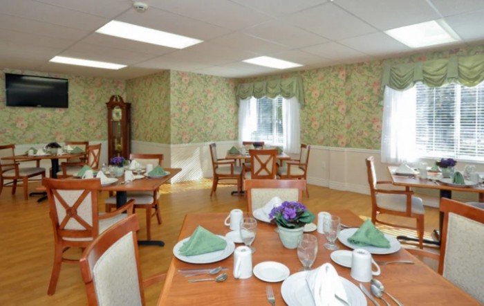 A well-lit dining room with neatly arranged tables and chairs, featuring elegant table settings and decorative wallpaper.