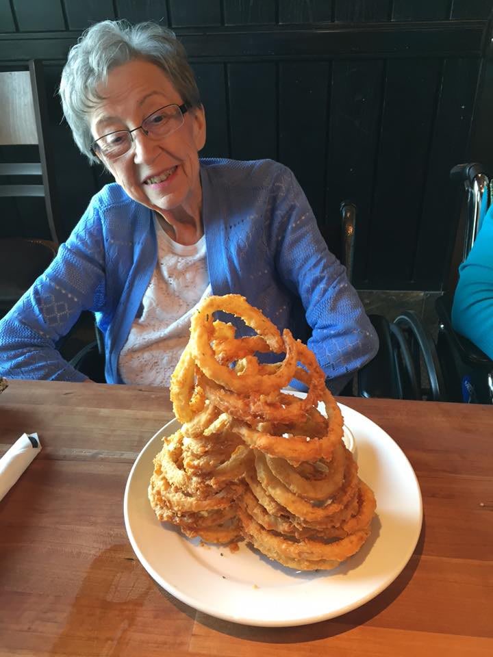 An elderly person sitting at a table in a restaurant with a plate of onion rings.