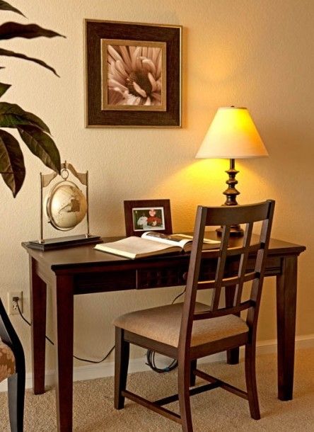 A cozy home office setup with a wooden desk, chair, and a lamp providing warm lighting.