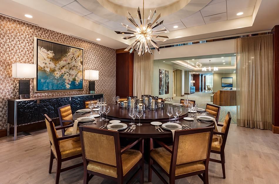 A luxurious dining room with a round table elegantly set for a meal, featuring a modern chandelier and sophisticated decor.