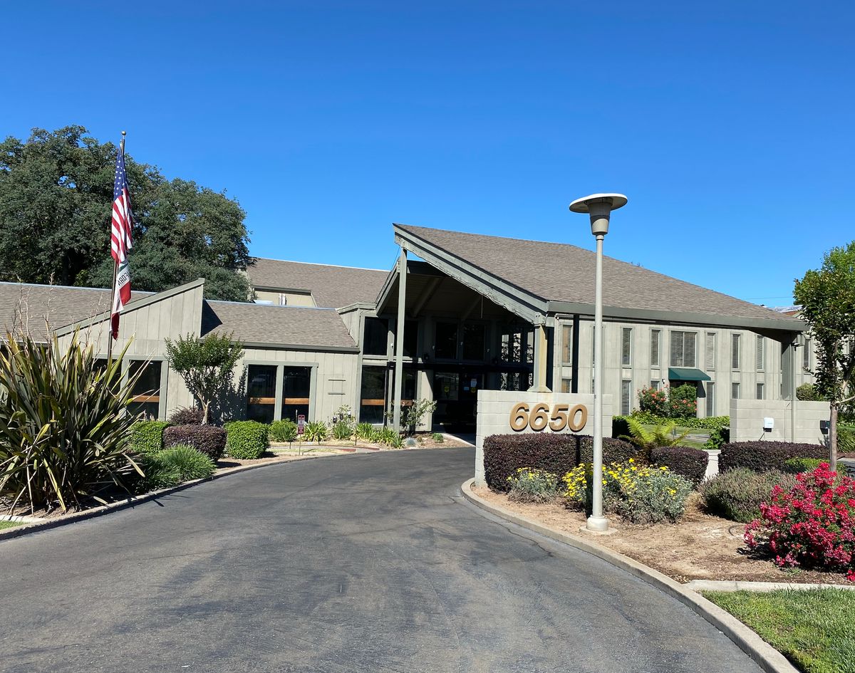 A modern office building with a driveway and landscaped surroundings under a clear blue sky.