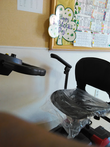 An office wheelchair partially wrapped in plastic, set against a wall with a calendar.