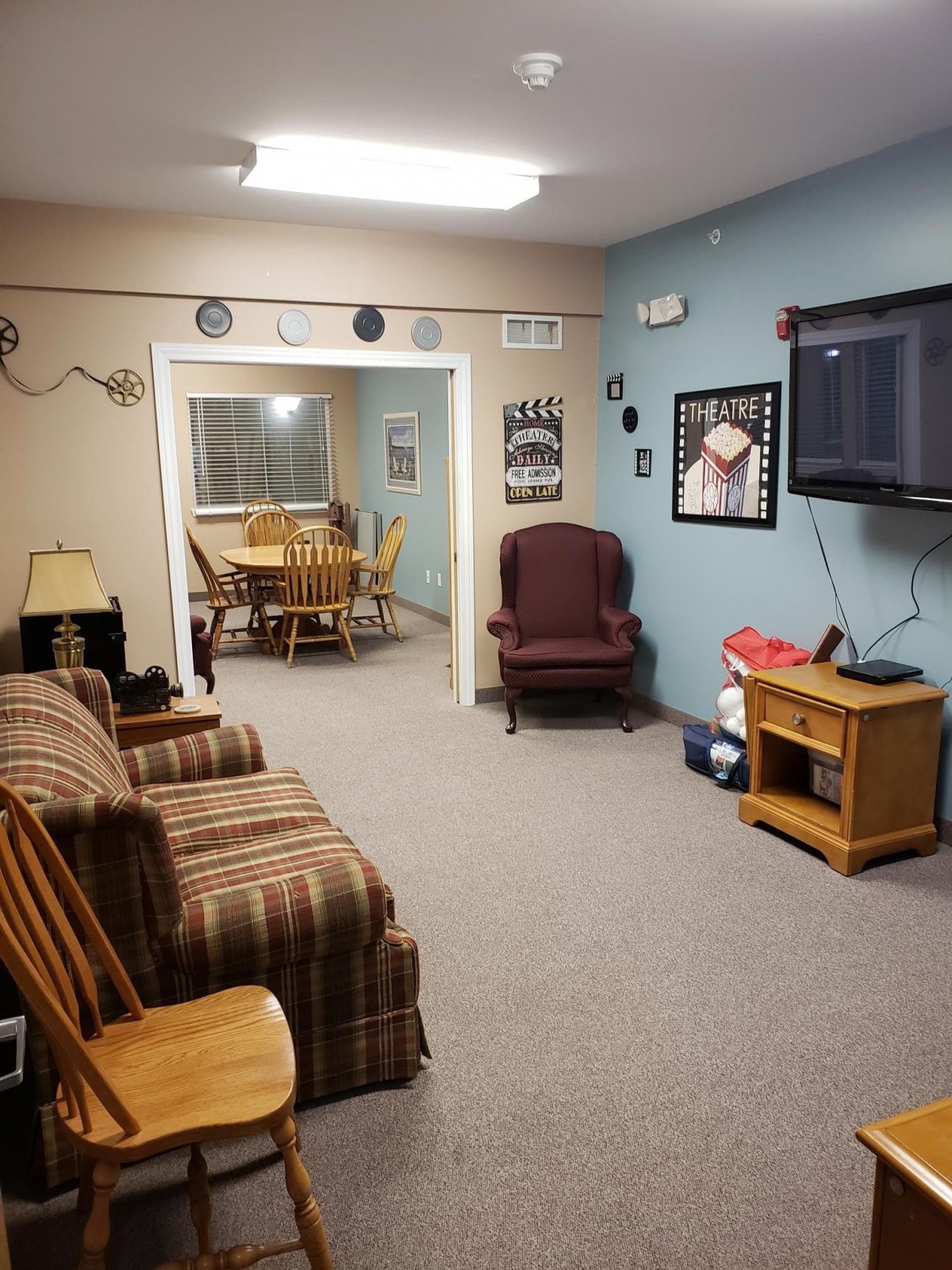 A cozy living room area with a sofa, chairs, a television mounted on the wall, and a dining table in the background.
