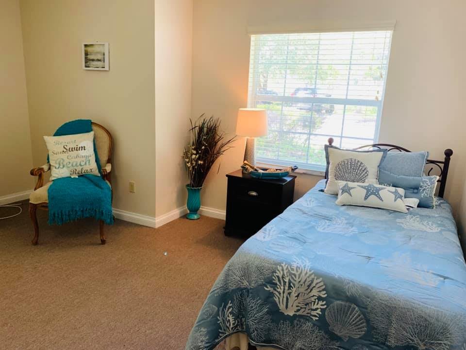 A cozy bedroom with a bed, chair, and lamp near a window.