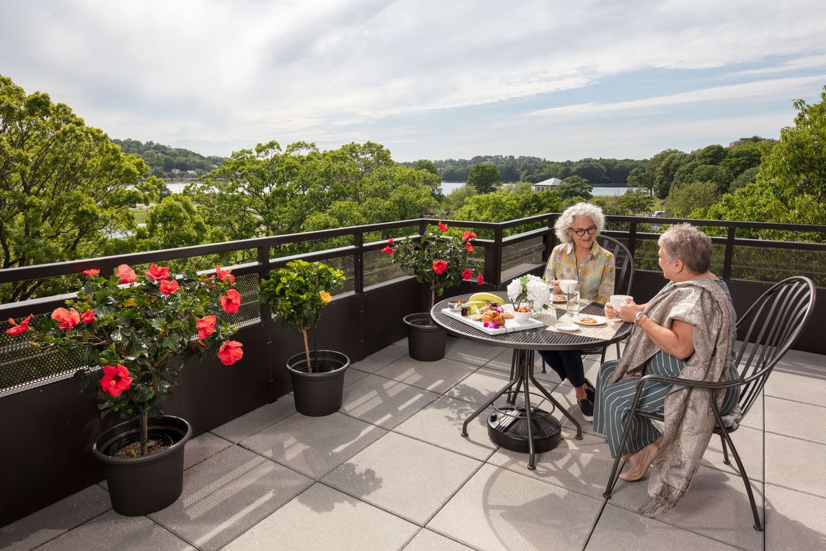 Two people enjoying a conversation on a scenic balcony with flowers and a view of the lake.