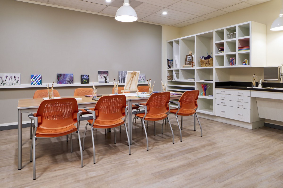 A modern meeting room with orange chairs and a large table surrounded by shelves filled with books and storage items.