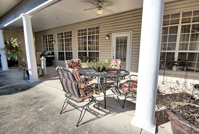 A cozy outdoor patio area with a metal table and cushioned chairs, accompanied by a ceiling fan, set against the backdrop of a house exterior with glass doors.