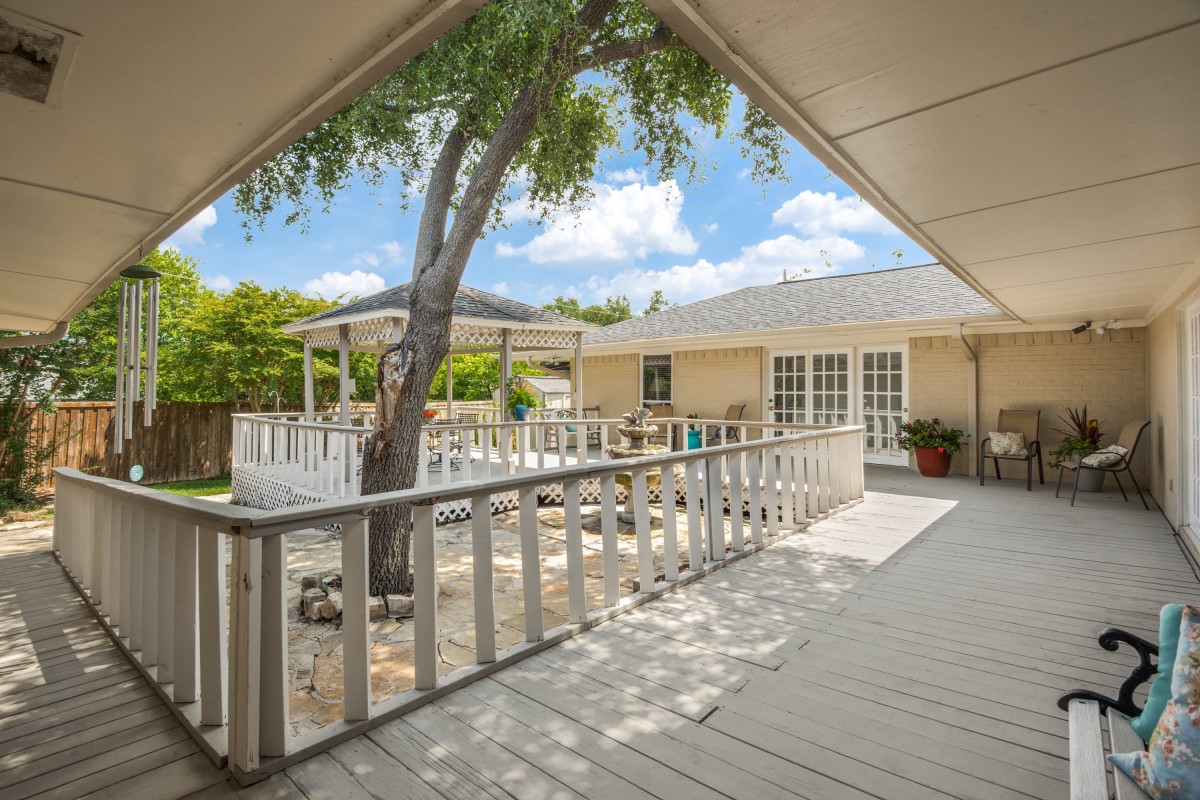 A spacious backyard deck with a tree growing through it, featuring a fenced area and patio under a sunny sky.