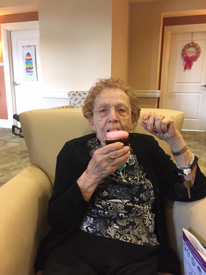 An elderly woman enjoying a cupcake while seated in a comfortable indoor setting.
