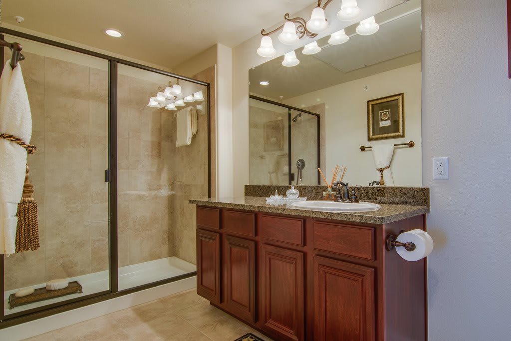 A well-appointed bathroom featuring a glass-enclosed shower, a large mirror above the sink, and elegant lighting fixtures.
