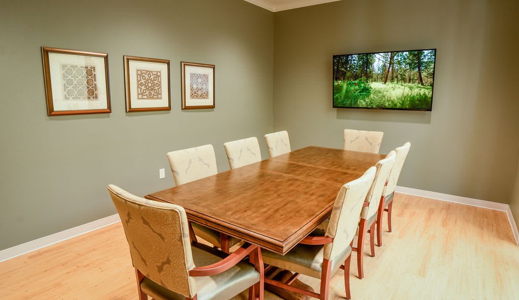 A well-furnished conference room with a large meeting table surrounded by chairs, decorative artwork on the walls, and a television screen displaying nature imagery.