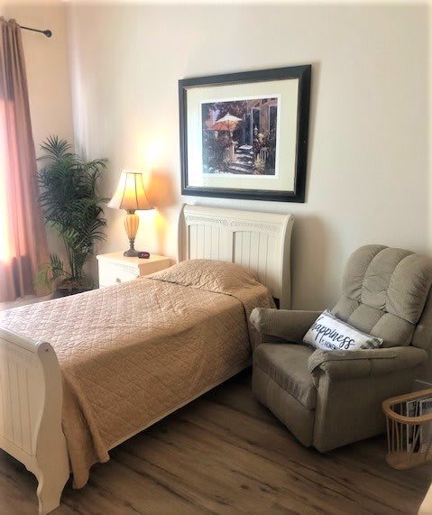 A cozy bedroom with a single bed, comfortable armchair, and warm lighting from a table lamp.