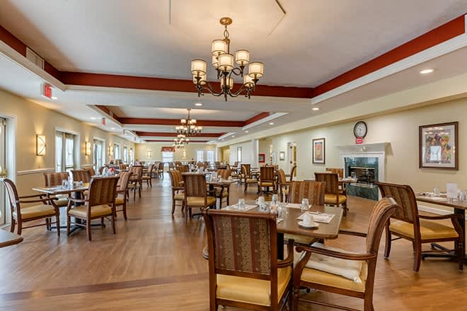 A spacious dining room with elegant chandeliers, neatly arranged tables, and comfortable chairs.