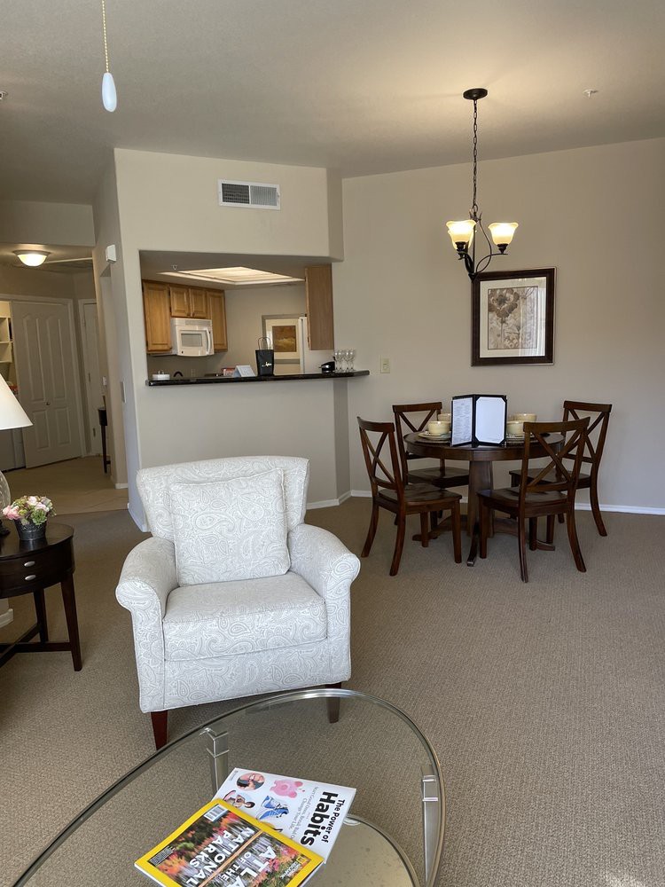 A cozy living room with an armchair, a dining table with chairs, and an open view of the kitchen.